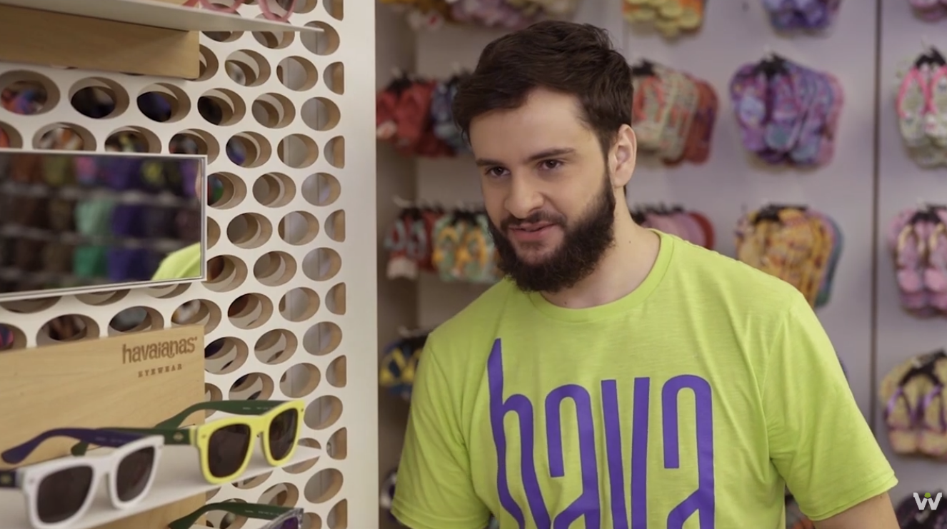 Ator interpretando vendedor da Havaianas próximo ao expositor de óculos